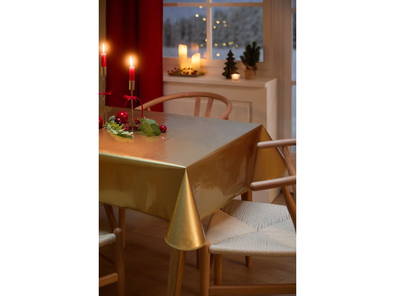 Feestelijke eettafel met gouden tafelkleed, rode kaarsen en kerstdecoraties.