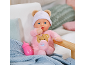 Zachte babypop in roze kruippakje en muts met berenoren naast een flesje.