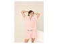 Vrouw in roze tweedelige pyjama met bloemenpatroon, poserend met haar handen achter haar hoofd.