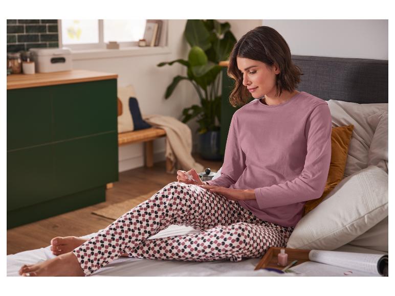 Een vrouw in roze pyjama met een gestreept patroon,  zit op bed en doet haar nagels.