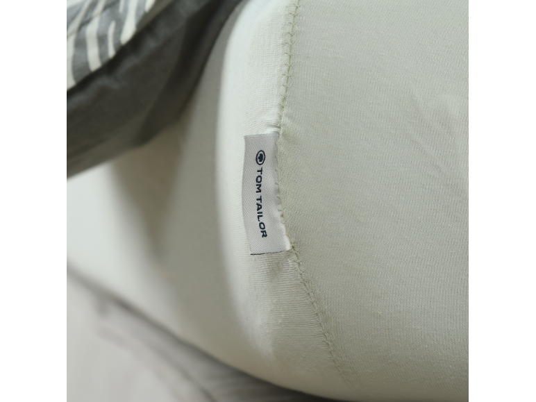 Close-up van een lichtgroen textiel met een wit etiket met zwarte tekst.
