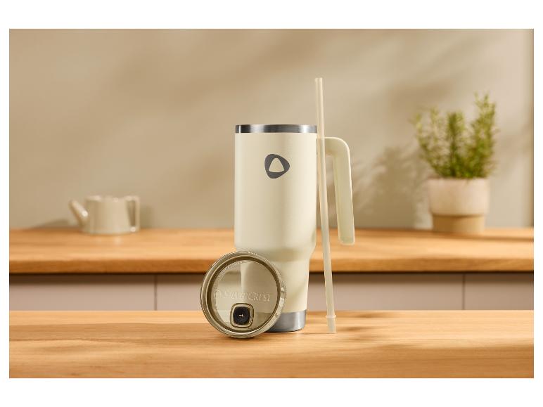 Crèmekleurige thermosbeker met handvat, deksel en rietje op een houten aanrecht.