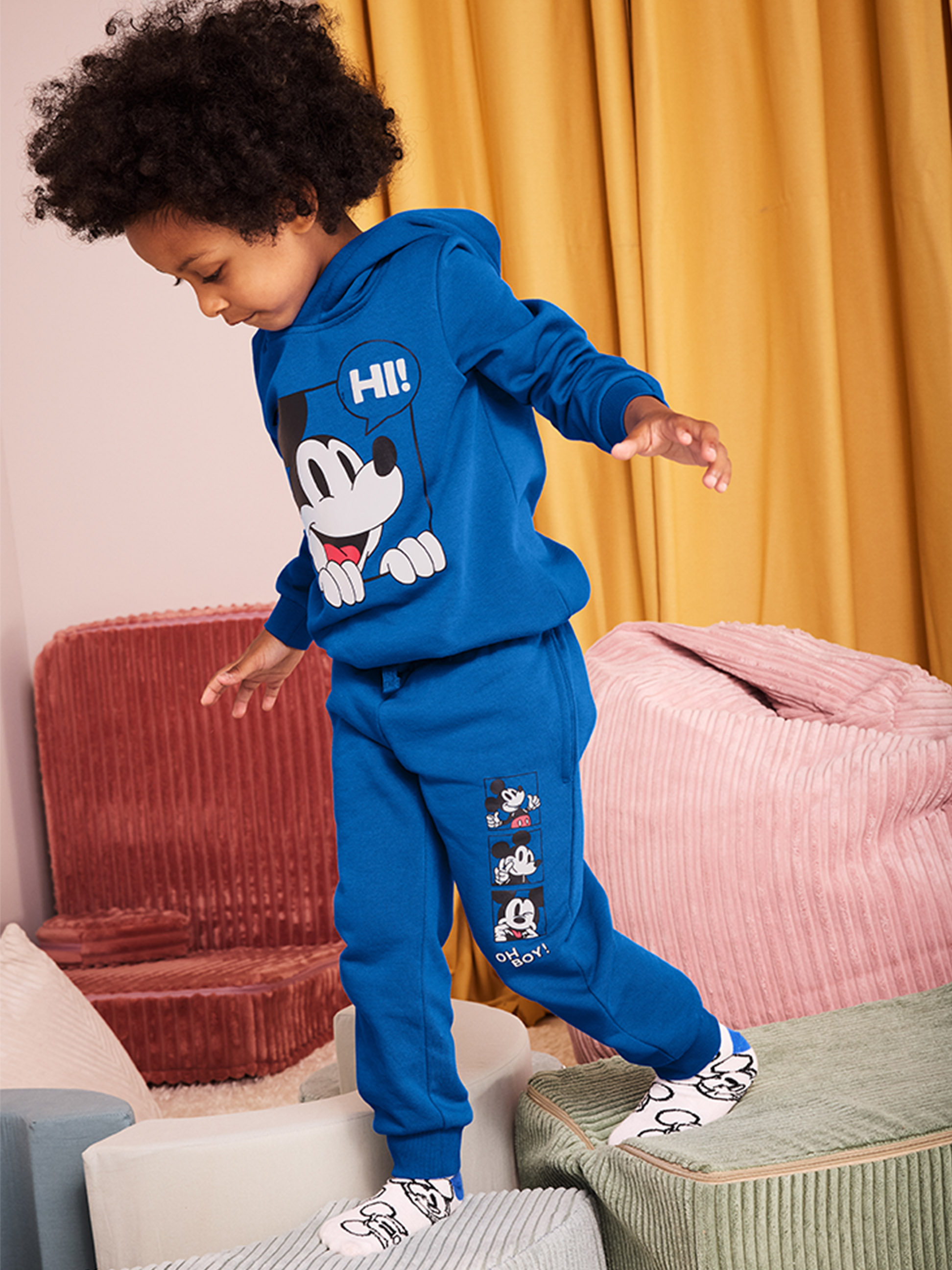 Een kind in een blauwe Mickey Mouse hoodie en joggingbroek stapt op zachte blokken.