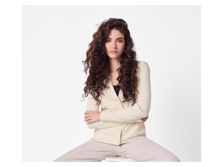 Vrouw in beige vest en broek zittend op een kruk.