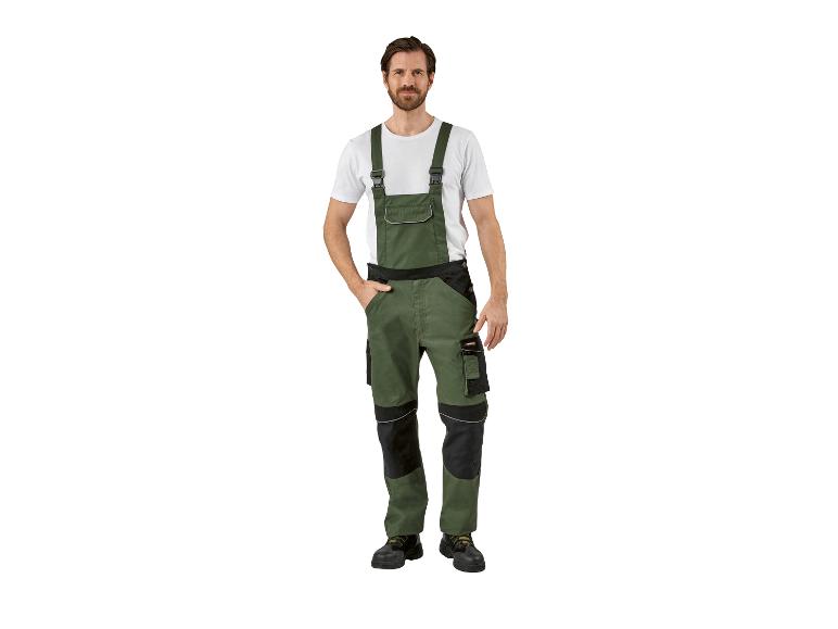 Een man modelleert een olijfgroene werkoverall met zwarte accenten en een wit t-shirt.
