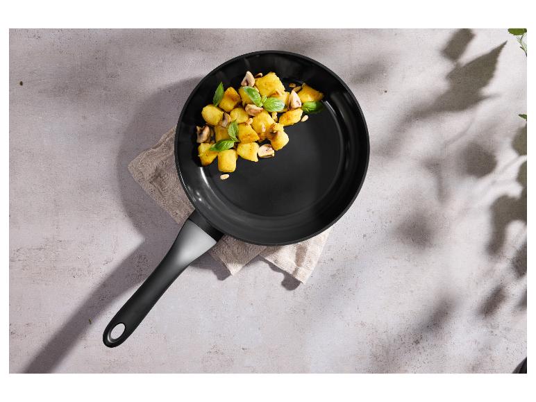 Koekenpan met gebakken aardappelen, champignons en basilicum op een lichte achtergrond.