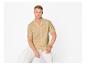 Man in beige overhemd met korte mouwen en witte broek, zittend op een witte achtergrond.