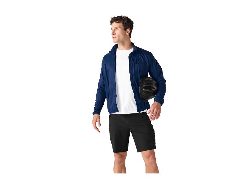 Man in blauwe jas, wit T-shirt en zwarte korte broek met fietshelm.