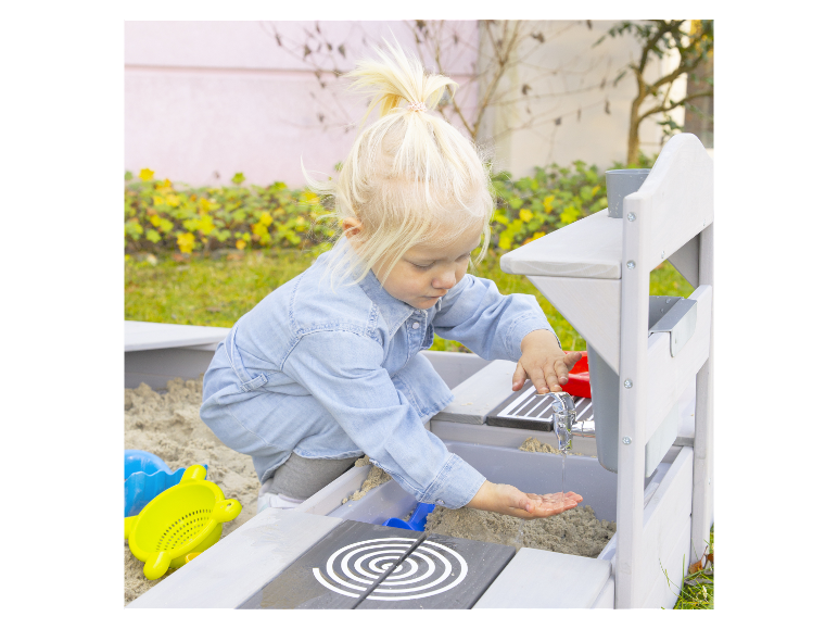 Een klein meisje speelt in een zandbak met een waterkraan en speelgoed.