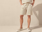 Man draagt gestreepte linnen shorts en beige sneakers.