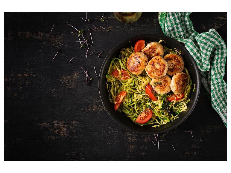 Kipburgers met courgettenoedels en tomaten in een zwarte pan.