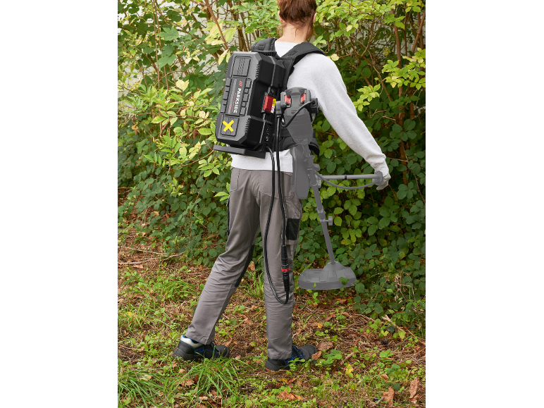 Persoon met rugzakaccu en grastrimmer in een tuin.
