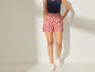 Vrouw draagt rode shorts met wit patroon en witte sneakers.
