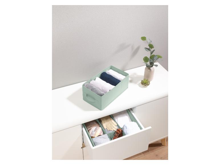 Een groene opbergdoos met kleding, op een wit dressoir met een open lade met andere opbergdozen.