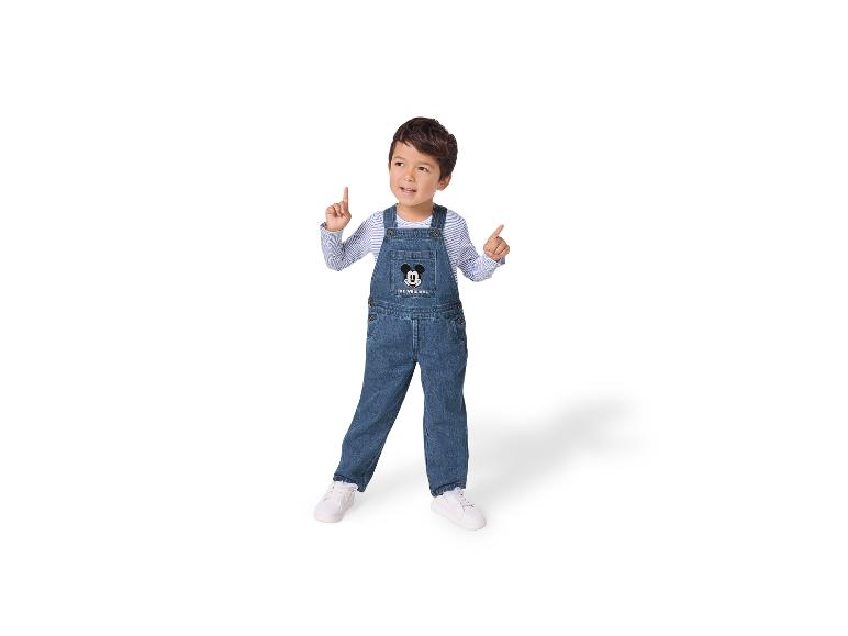 Jongen in Mickey Mouse spijkerbroek en gestreept shirt met lange mouwen, wijzend omhoog.
