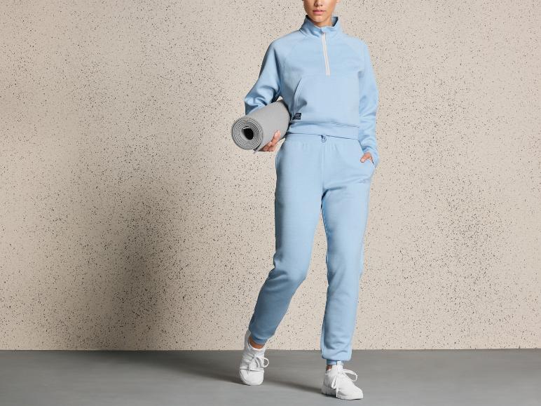 Een vrouw in een blauwe trainingsbroek en trui met een yogamat.