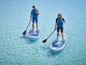 Twee personen peddelen op blauwe Red Paddle Co. sup boards in turquoise water.