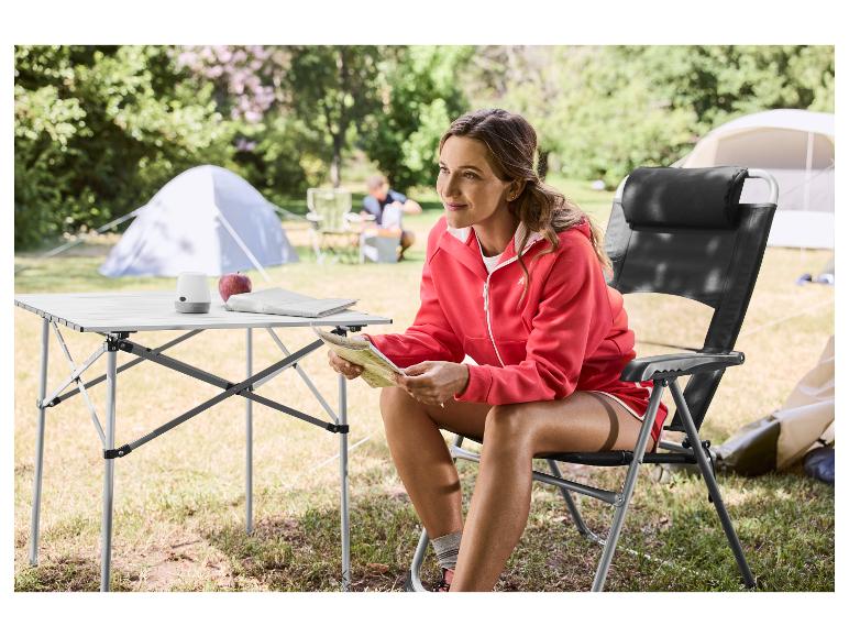 Vrouw zit op een campingstoel naast een campingtafel, met een kaart.
