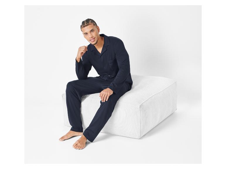 Man in een donkerblauwe pyjama zit op een witte poef.