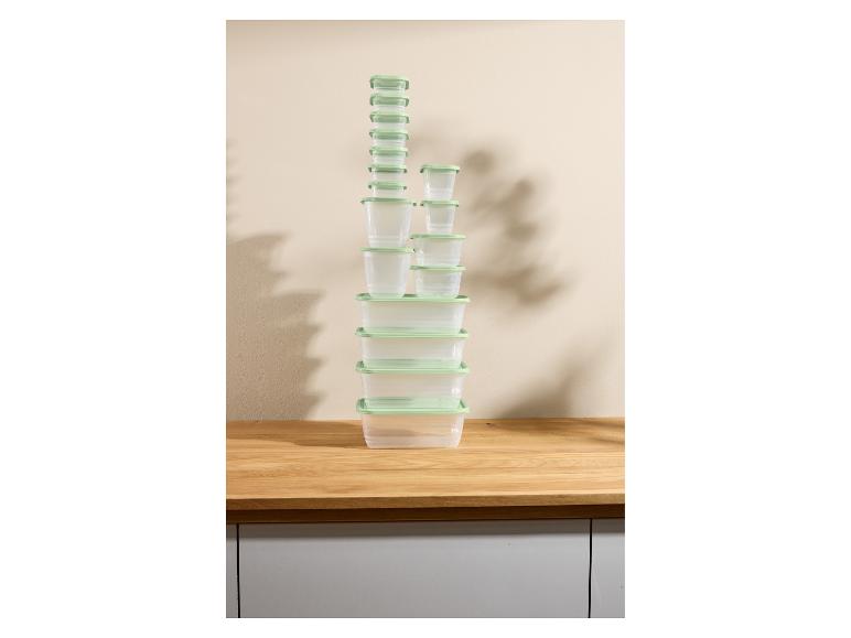 Een hoge stapel doorzichtige plastic voedselcontainers met lichtgroene deksels op een houten aanrecht.