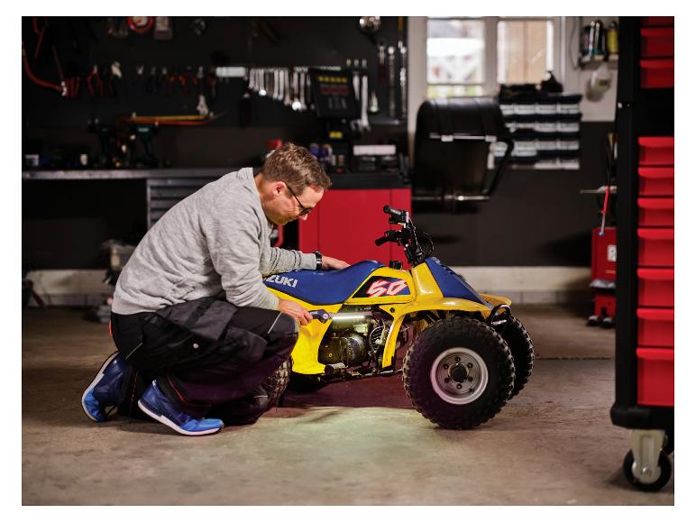 Man met LIVARNO® werklamp „The Mechanic“ repareert gele quad.