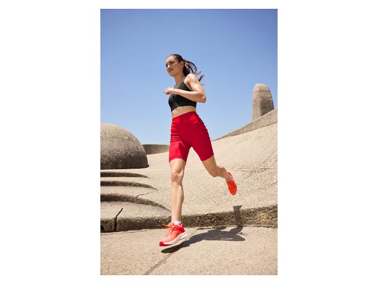 Vrouw in zwarte sportbeha en rode fietsbroek rent buiten.