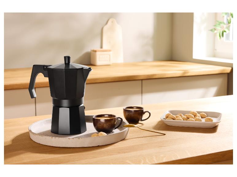 Zwart koffiezetapparaat, twee kopjes koffie en koekjes op een houten tafel.