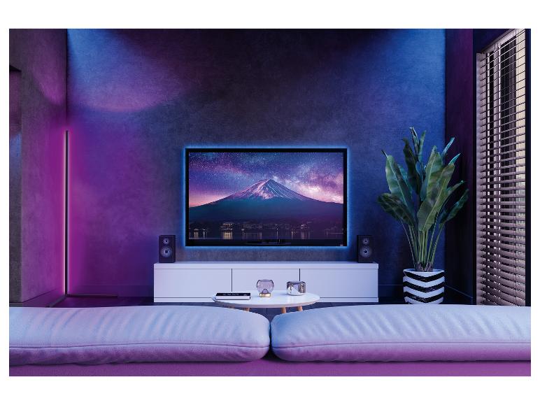 Woonkamer met tv, tv-meubel, luidsprekers, plant en bank, verlicht met paars en blauw licht.