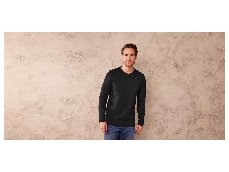 Man draagt een zwart T-shirt met lange mouwen en blauwe jeans.