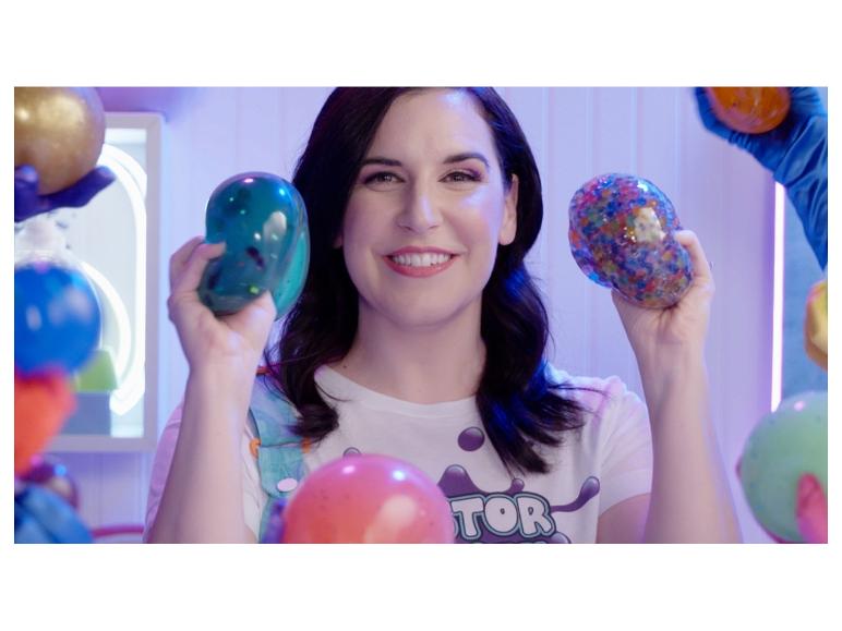 Lachende vrouw houdt twee squishy speeltjes vast, één blauw en één veelkleurig.