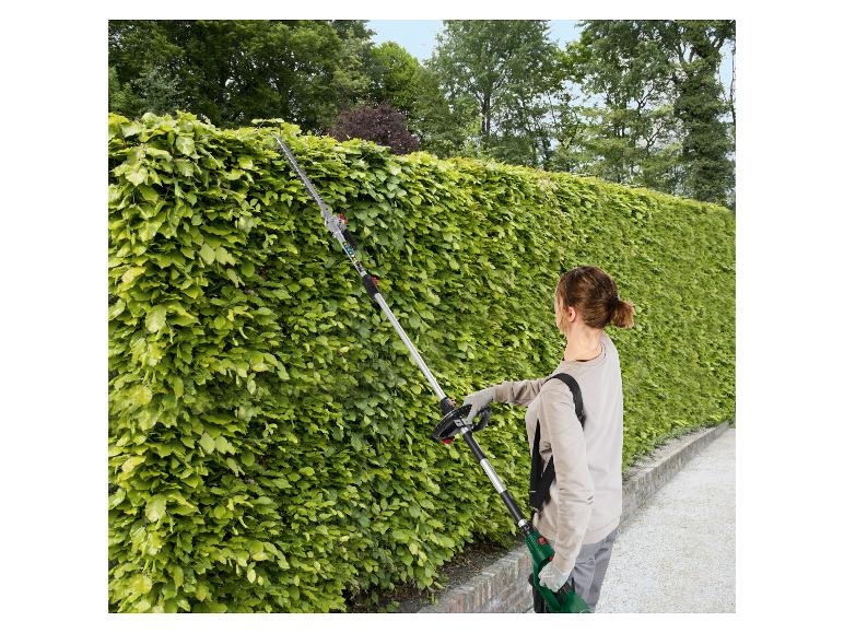 Een vrouw gebruikt een lange STIHL heggenschaar om een hoge haag te snoeien.
