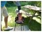 Man giet gloeiende kolen in een houtskoolbarbecue in de tuin, picknicktafel op de achtergrond.