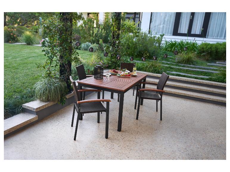 Buiten eethoek met houten tafel en rieten stoelen op een terras met uitzicht op de tuin.