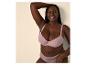 Lachende vrouw in roze beha en slip, met hand achter haar hoofd.