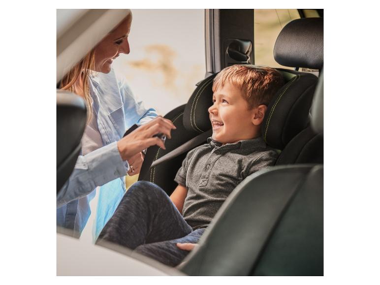 Een lachende vrouw zet een kind vast in een kinderautostoel.