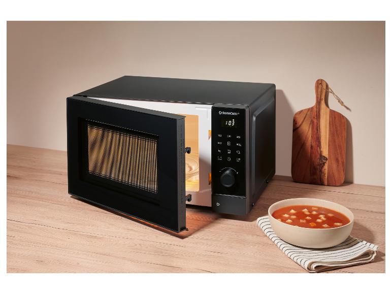 Zwarte magnetron met open deur en kom soep op een houten aanrecht.