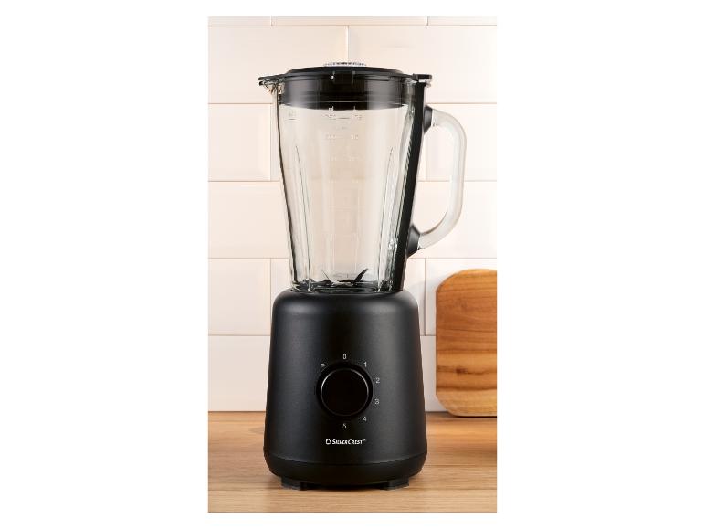 Zwarte blender met glazen kan, bedieningsknop en maatstreepjes op een houten ondergrond.