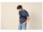 Man in blauw T-shirt, donkerblauwe trui om de schouders geknoopt en lichte jeans.