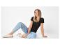 Vrouw in een zwart T-shirt en lichtblauwe jeans, zittend op de grond, lachend.