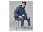 Man in een blauwe hoodie en bijpassende joggingbroek, zittend op een kruk.