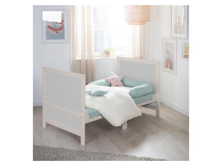 Wit houten babybed met mintgroen beddengoed en stervormige kussens in een lichte kamer.