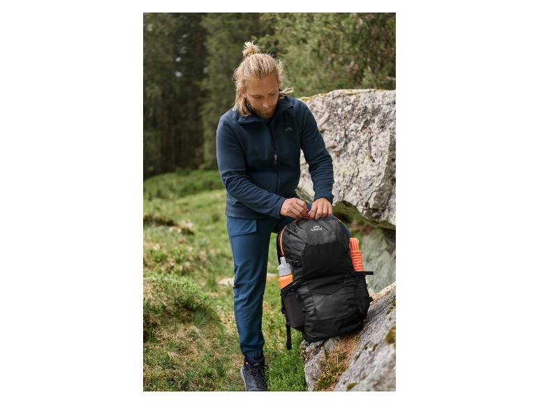 Man in donkerblauwe fleecejas en broek pakt een zwarte rugzak met oranje details in.