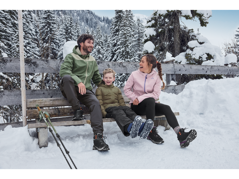 Familie in winterjassen en wandelschoenen zit op een besneeuwde bank, genietend van het winterlandschap.