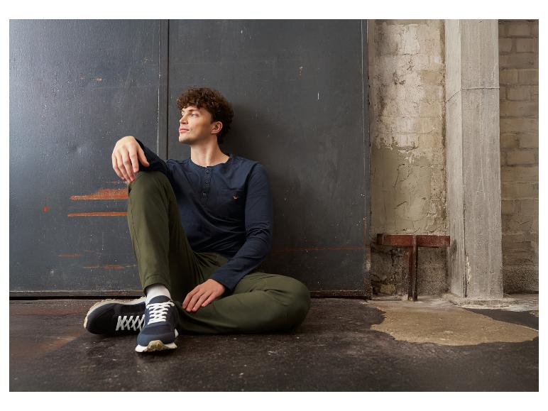 Man in donkerblauw shirt met lange mouwen en groene broek, zittend op de grond.