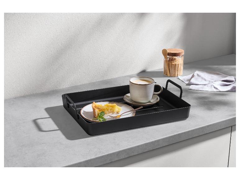 Zwart dienblad met koffiekopje en stuk taart op een aanrecht.