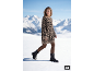 Vrouw in luipaardprint trui-jurk en zwarte laarzen loopt door de sneeuw, bergen op de achtergrond.