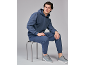 Man in een marineblauw trainingspak en grijze sneakers, zittend op een kruk.