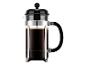 French press koffiezetapparaat met donkere koffie en drab, zwarte deksel en handvat, en een chromen frame.