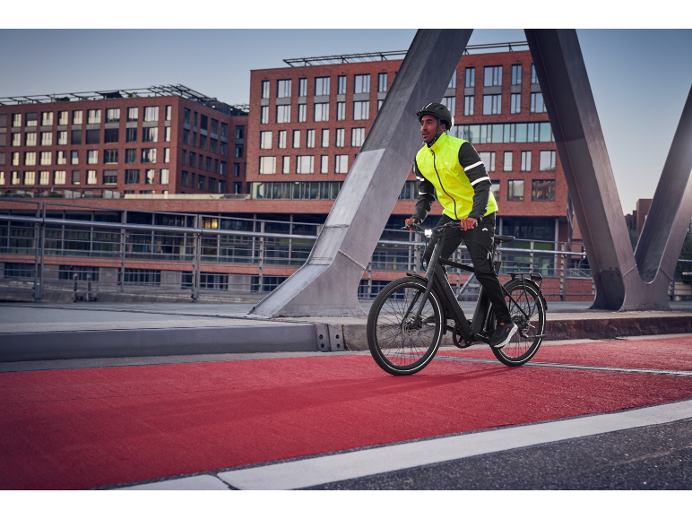 Man in fietsjack en helm rijdt op e-bike op rood fietspad.