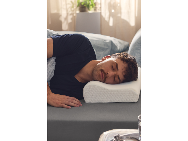 Man slaapt op zijn zij op grijs beddengoed, met zijn hoofd op een ergonomisch kussen.